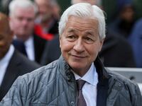 Jamie Dimon waves his hand and smirks outdoors.