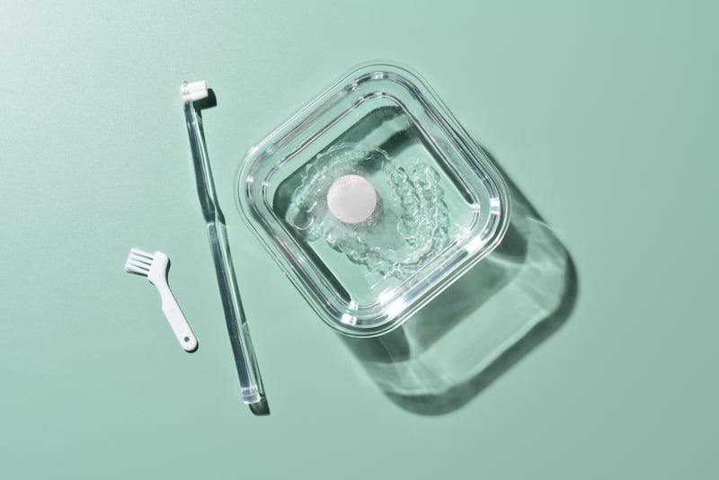 Cleaning Invisible Braces by Using Brushes With Effervescent Tablet on Green Background Directly Above View.