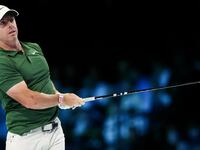 Rory McIlroy mid-swing with a driver, wearing a red and white WHOOP wearable on his left wrist, dressed in a green polo and white cap.
