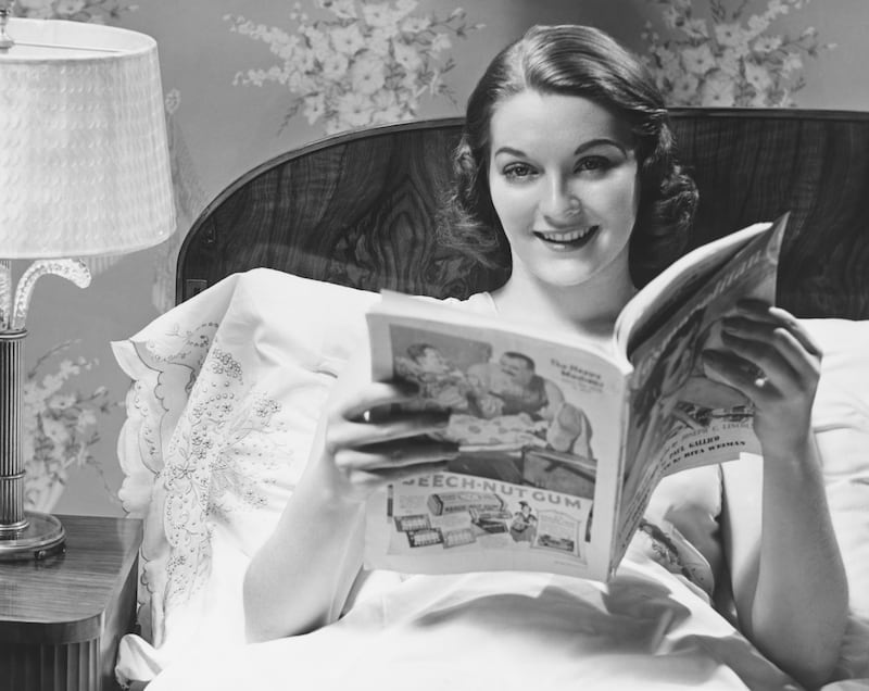 50s woman in bed, reading magazine