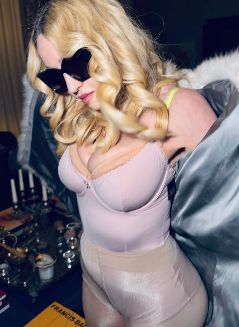 Madonna, wearing curls and sunglasses, opening a blue and white fur coat to reveal pink lingerie