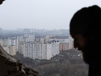 A photo of the view of a Russian city through the rubble of another building. A man’s silhouette can be seen through the view.