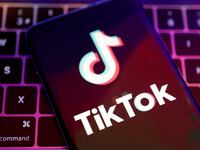 TikTok logo is on a phone placed over a laptop keyboard.