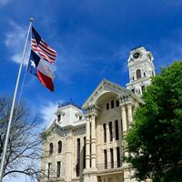American and Texas flags fly in front of the Hill County courthouse in Hillsboro Texas.