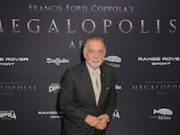 Francis Ford Coppola stands in front of a promotional background at the premiere of his film “Megalopolis”.
