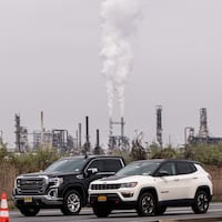 A photo of greenhouse gases being emitted from a pair of tall smokestacks in an industrial area.