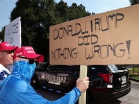 A supporter of former President Donald Trump holds a banner at the entrance of the Fulton County Jail, as Trump is expected to turn himself in to be processed after his Georgia indictment, in Atlanta, Georgia.