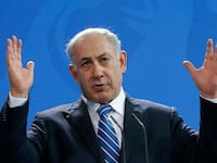 Benjamin Netanyahu speaks on stage with his hands raised.