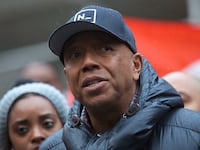 Russell Simmons, wearing a hat, prepares to speak at an outside event.