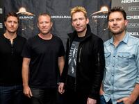 A photo of the band Nickelback standing in front of a step and repeat.