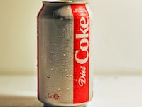 A sweating can of Diet Coke on a white surface against a white background.