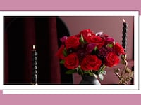 Romantic Valentine’s Day floral arrangement from 1-800-Flowers featuring red roses in a modern vase, styled with black taper candles for an elegant at-home setting.