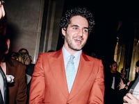 Benny Safdie wears a suit and is talking to two men at a party.