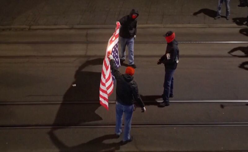 Masked protesters burn a U.S. flag, held upside down, in the street.