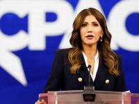 Kristi Noem gives a speech at a podium with a CPAC lego behind her