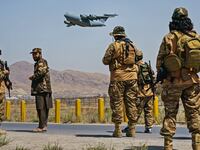 A photo of Taliban soldiers patrolling a street while a US aircraft flies off in the distance
