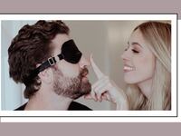 A couple enjoying a playful moment, with the man wearing a black blindfold and the woman smiling while gently touching his nose.