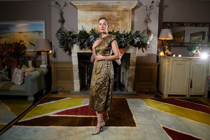 Rosamund Pike poses for a picture in front of a fireplace.