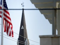 An American Flag flies in front of a church steeple.