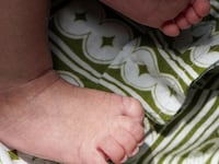 A heartwarming close-up shot focusing on the delicate, wrinkled feet of a sleeping infant, resting comfortably on a richly patterned fabric of olive green and white stripes and clover-like designs und