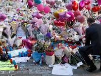 A man crouches in front of flowers, messages, and tokens left in tribute to the victims of the attact on Manchester Arena, in central Manchester, Britain, May 26, 2017.