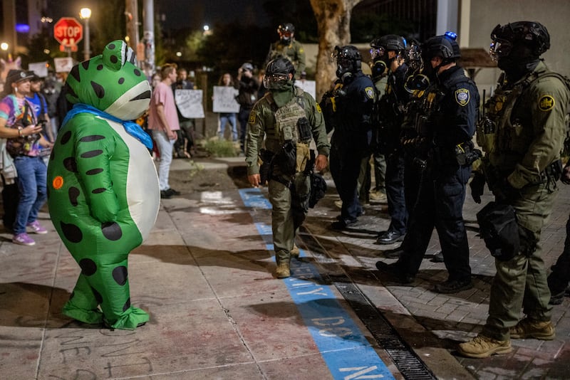 A protester in a frog costume stands in front of a line of federal law enforcement officers outside a United States Immigration and Customs Enforcement (ICE) facility in Portland,