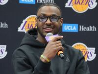 Bronny James smiles while holding a microphone at a Lakers press event.