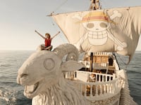 Luffy sits on the helm of a large white pirate ship.