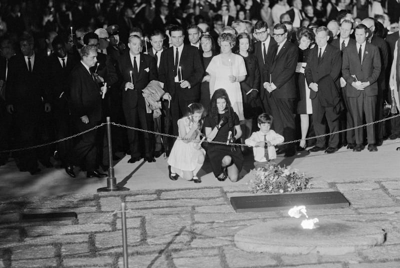 Jackie Kennedy and children Caroline and John kneel at the gravesite of husband and father President John Kennedy. Caroline prepares to place a flower there. The eternal flame is in the foreground and Kennedy family and friends taking part in the funeral service for the assassinated Bobby Kennedy are at rear. (Photo by © Wally McNamee/CORBIS/Corbis via Getty Images)