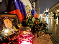 People walk past a portrait of Russian military blogger Vladlen Tatarsky, who was killed in a cafe explosion, with St. Basil’s Cathedral in the background in Moscow, Russia, April 4, 2023.