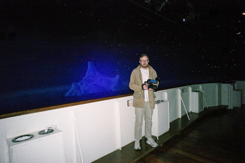A still from “How to with John WIlson” that shows John Wilson standing on a ship