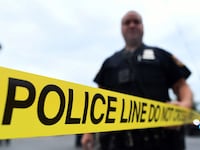 A photo of a police officer standing behind yellow crime scene tape.