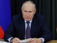 Russian President Vladimir Putin leans on desk at a meeting.
