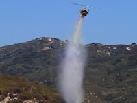 A helicopter drops water to extinguish a rapidly-growing brush fire in southern California.