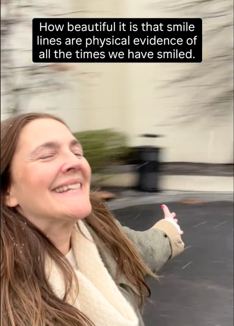 Drew Barrymore gleefully spins in circles, smiling, in a TikTok promoting natural aging and smile lines.