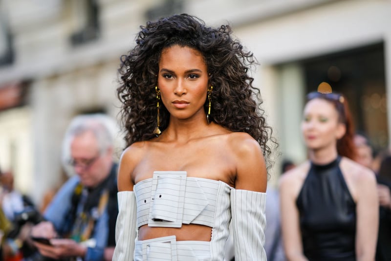 PARIS, FRANCE - JULY 06: Cindy Bruna wears gold long pendant earrings, a white gray with small black striped print pattern shoulder-off / large belted / long sleeves corset jacket from Jean-Paul Gaultier, matching white gray with small black striped print pattern wide legs suit pants, outside Jean-Paul Gaultier, during Paris Fashion Week - Haute Couture Fall Winter 2022 2023, on July 06, 2022 in Paris, France. (Photo by Edward Berthelot/Getty Images)
