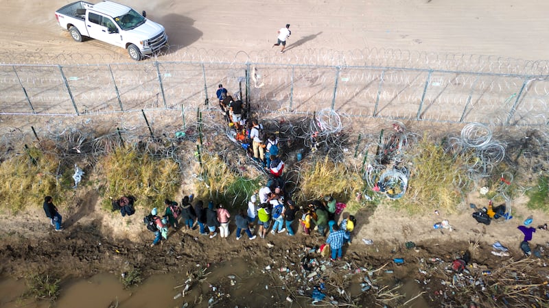 In an aerial view, immigrants pass through coils of razor wire while crossing the U.S.-Mexico border on March 13, 2024 in El Paso, Texas.