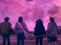 A group of four girls look up at a pink sky.