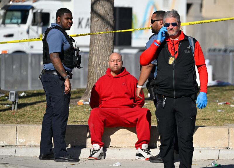A man, dressed in all red, sits in handcuffed, flanked by cops.