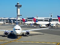 A Delta Airlines passenger jet taxis at John F. Kennedy International Airport in New York, New York, with the airport's 32 story, 321-foot tall control tower in the background.