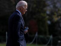 Joe Biden has his head down and phone in hand as he walks out of the White House.