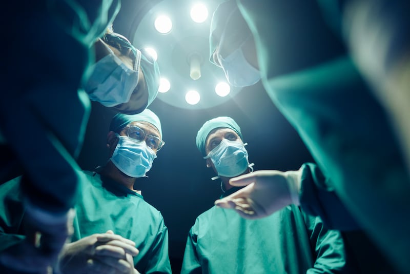 several doctors standing over a patient with a medical lamp above their heads