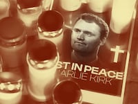 Photo illustration of a memorial of Charlie Kirk with candles obscuring a poster with "in peace" below his picture