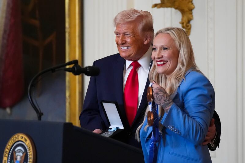 President Donald Trump holds an Order of Ikkos Olympic medal as he poses for a photo with Olympian bobsledder Kaillie Humphries and her bronze medals during a Women's History Month event in the East Room of the White House on March 12, 2026.