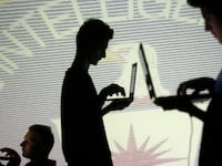 People are silhouetted as they pose with laptops in front of a screen projected with binary code and a Central Inteligence Agency (CIA) emblem, in this picture illustration taken in Zenica