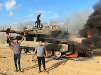 Palestinians cheer as an Israeli military vehicle burns after it was hit by Palestinian gunmen