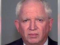 John Eastman stares forward in a mugshot, wearing a suit and tie.