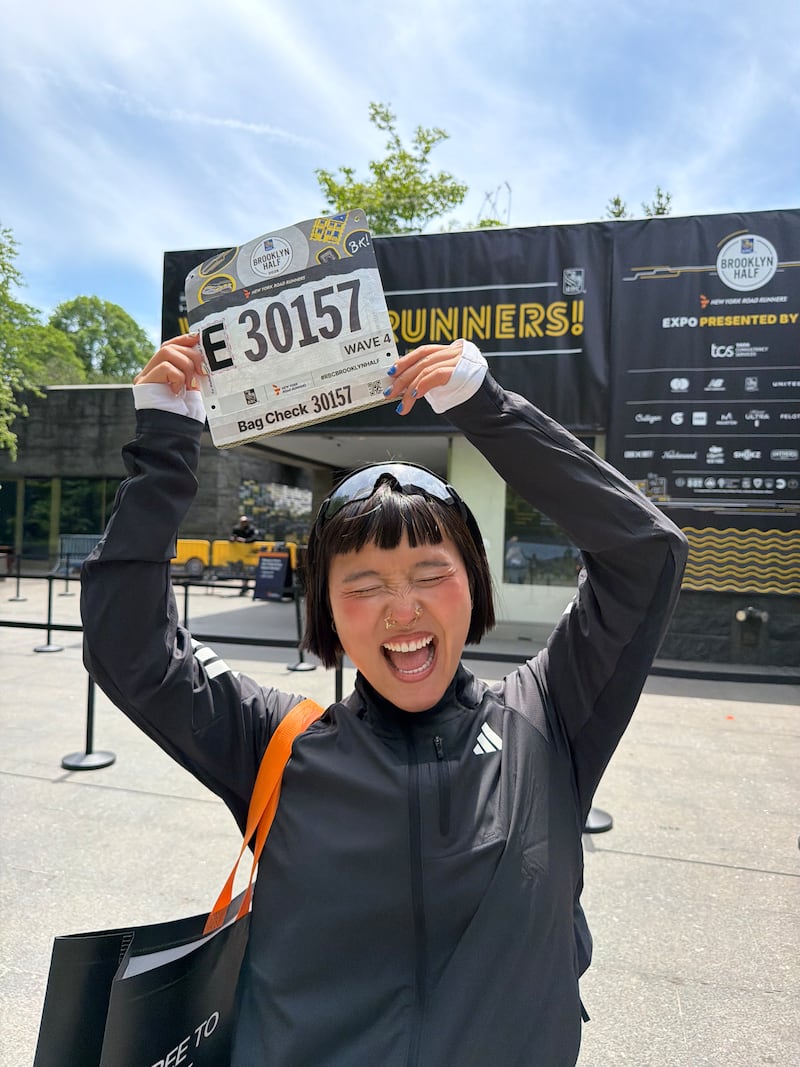 Ameya Okamoto poses excitedly with her bib for the Brooklyn Half Marathon.