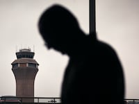 NEWARK, NEW JERSEY - MAY 6: A man stands outside Terminal C with the airport control tower in the background at Newark Liberty International Airport, on May 6, 2025 in Newark, New Jersey. Passengers traveling to, from, or through Newark Liberty International Airport (EWR) have experienced several days of delays and cancellations caused by air traffic control staffing shortages and equipment malfunctions.(Photo by Andres Kudacki/Getty Images)