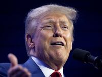 Donald Trump speaks with his hand raised on stage at a TPUSA event in July.